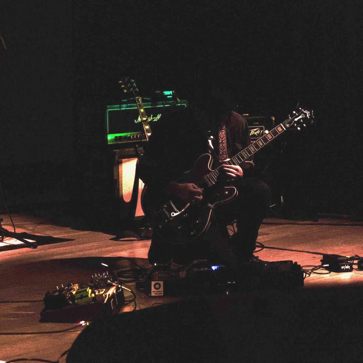 Guitarrista agachado no chão do palco mexendo nos pedais