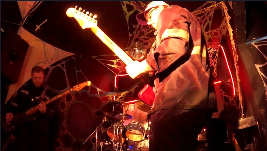 Guitarrista tocando sob luz vermelha diante de um painel de teias